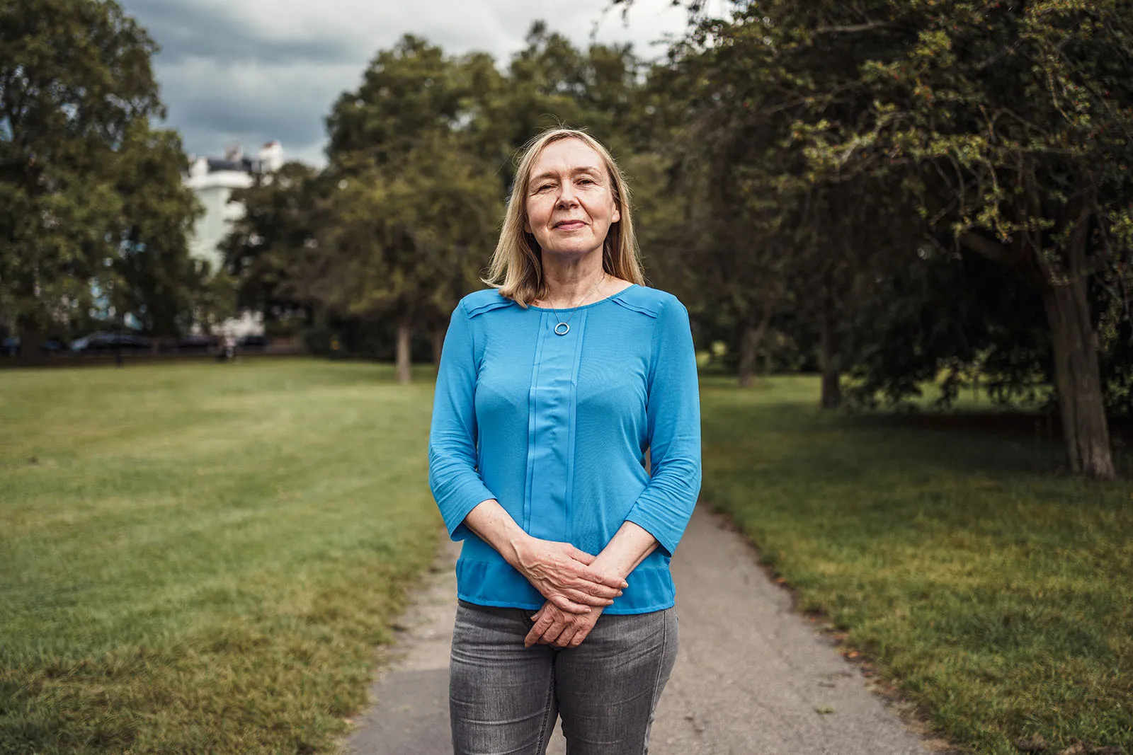 Portrait of woman stood in a park wearing blue top and jeans looking directly into camera
