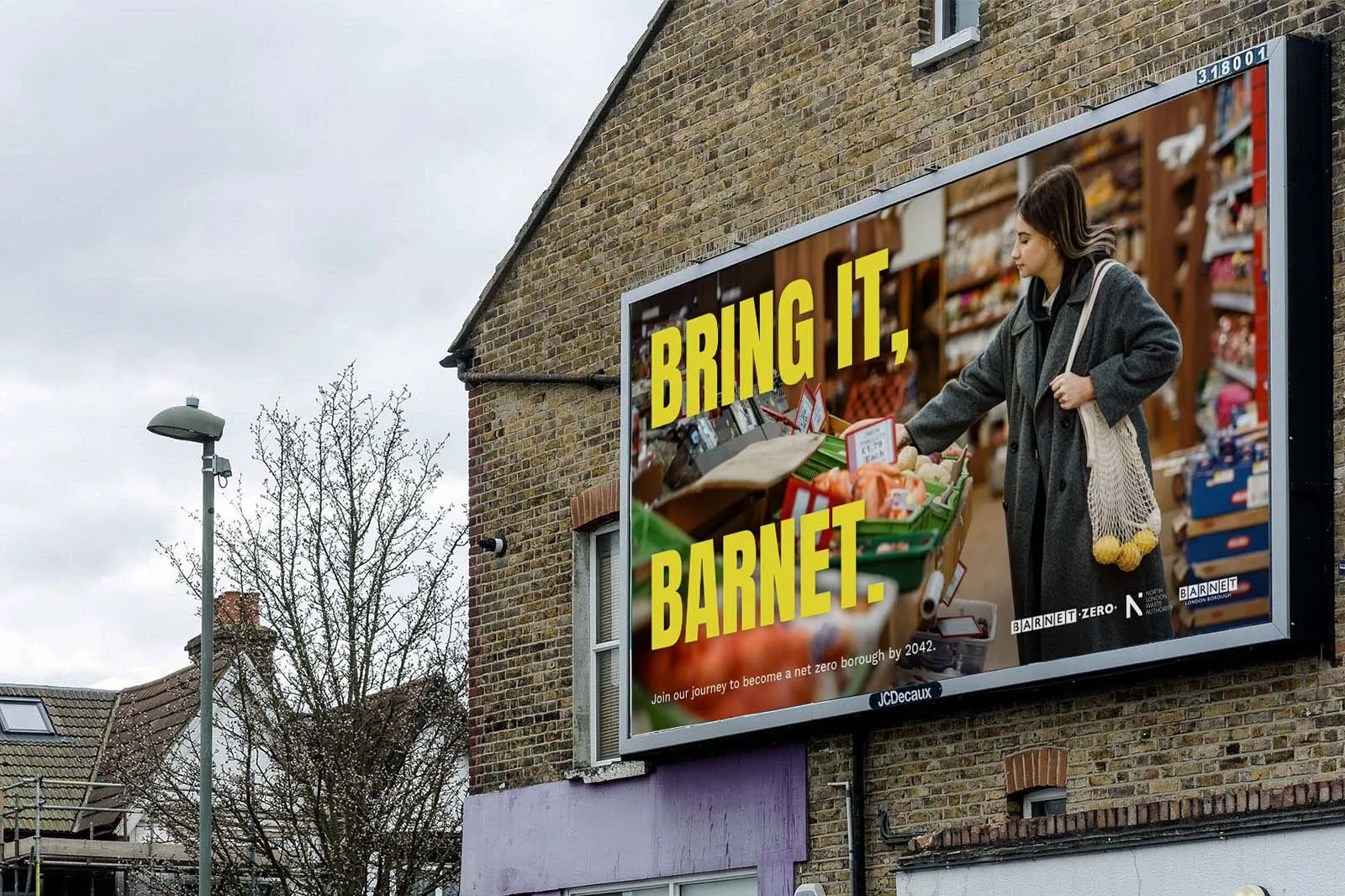 A billboard on a brick building shows a woman shopping in a grocery store with the text "BRING IT, BARNET." in bold yellow letters.