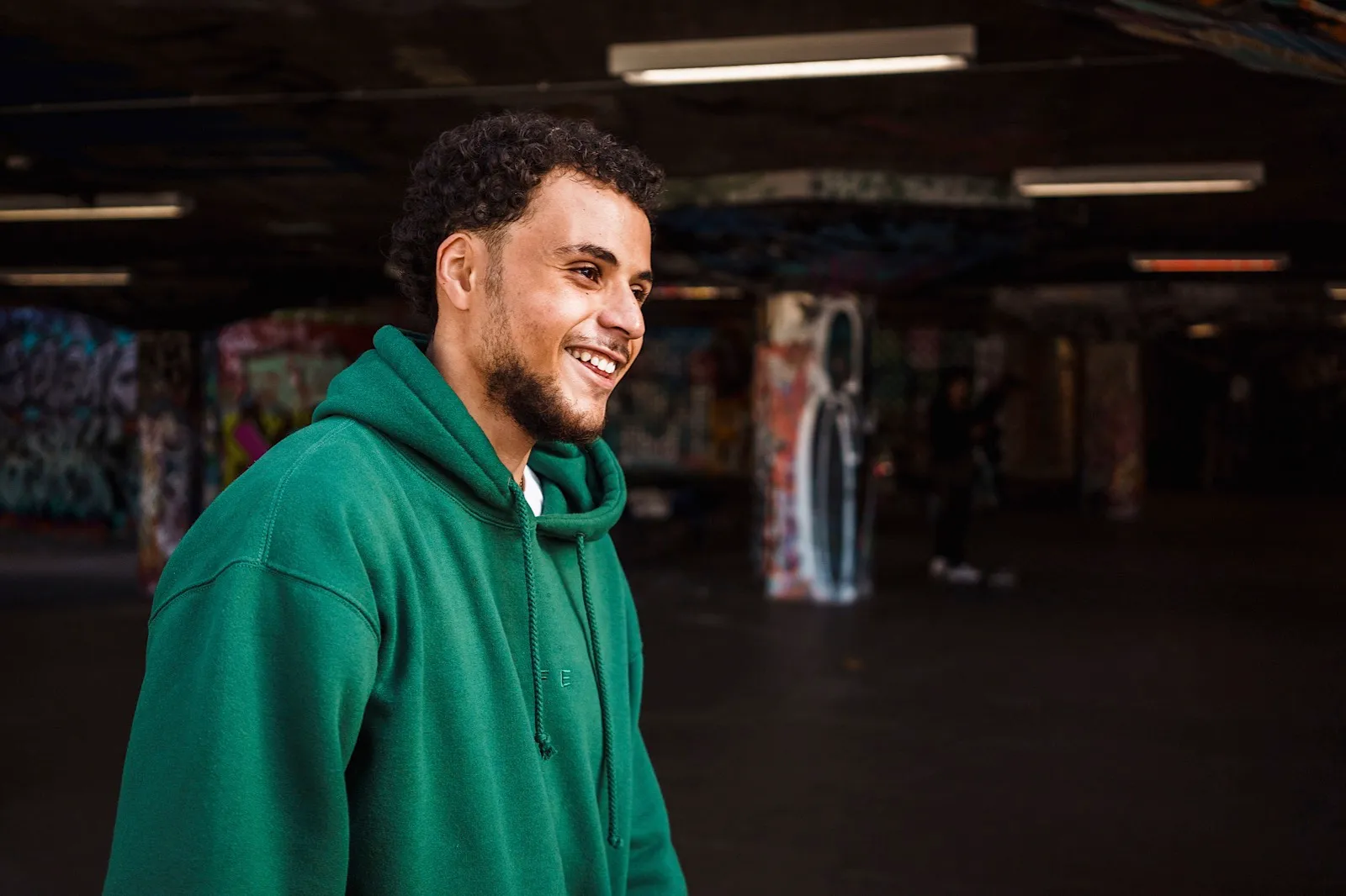 Man in green hoodie at skate park grinning