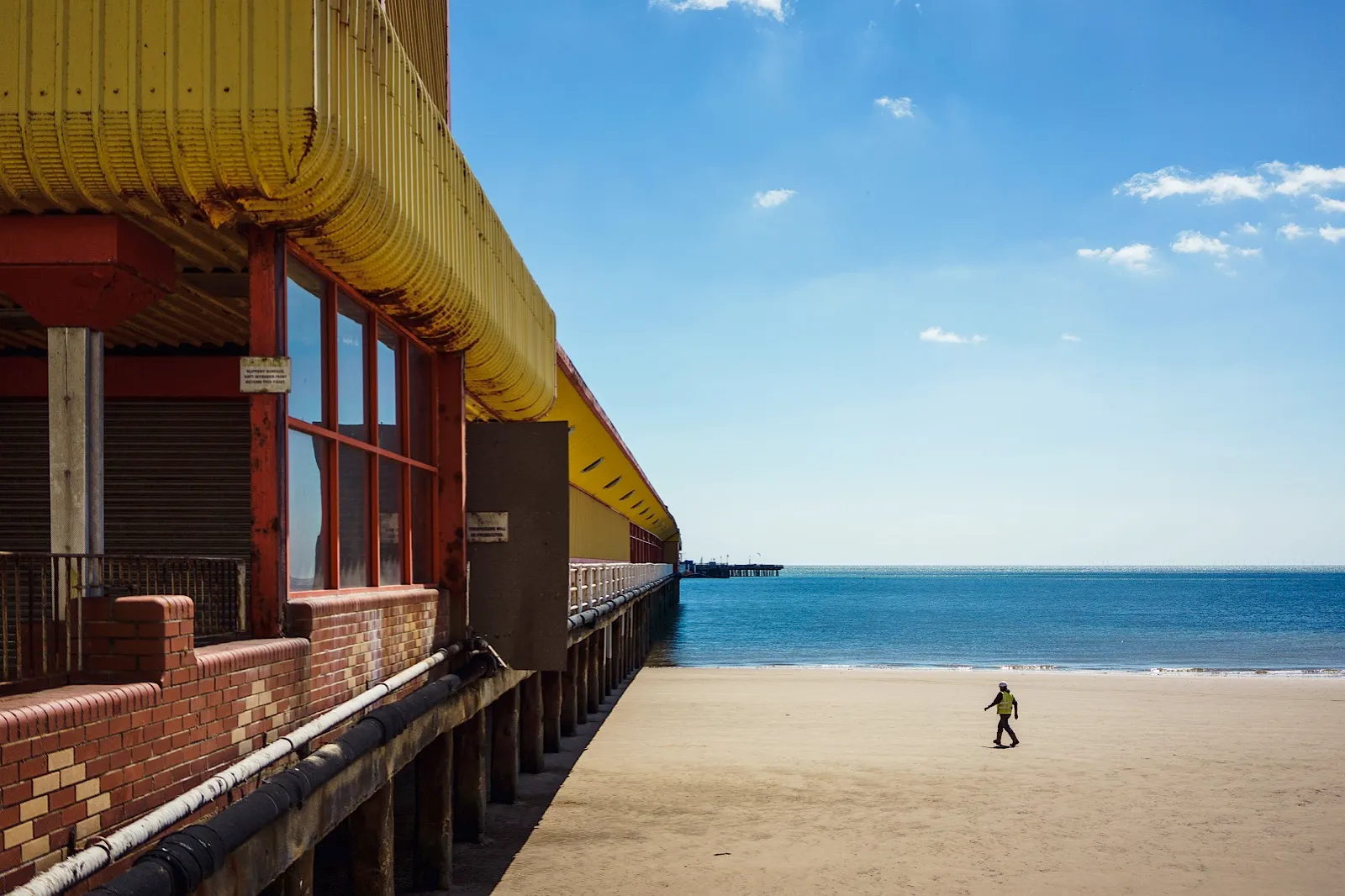 Man walking on the beach towards the underside of the pier
