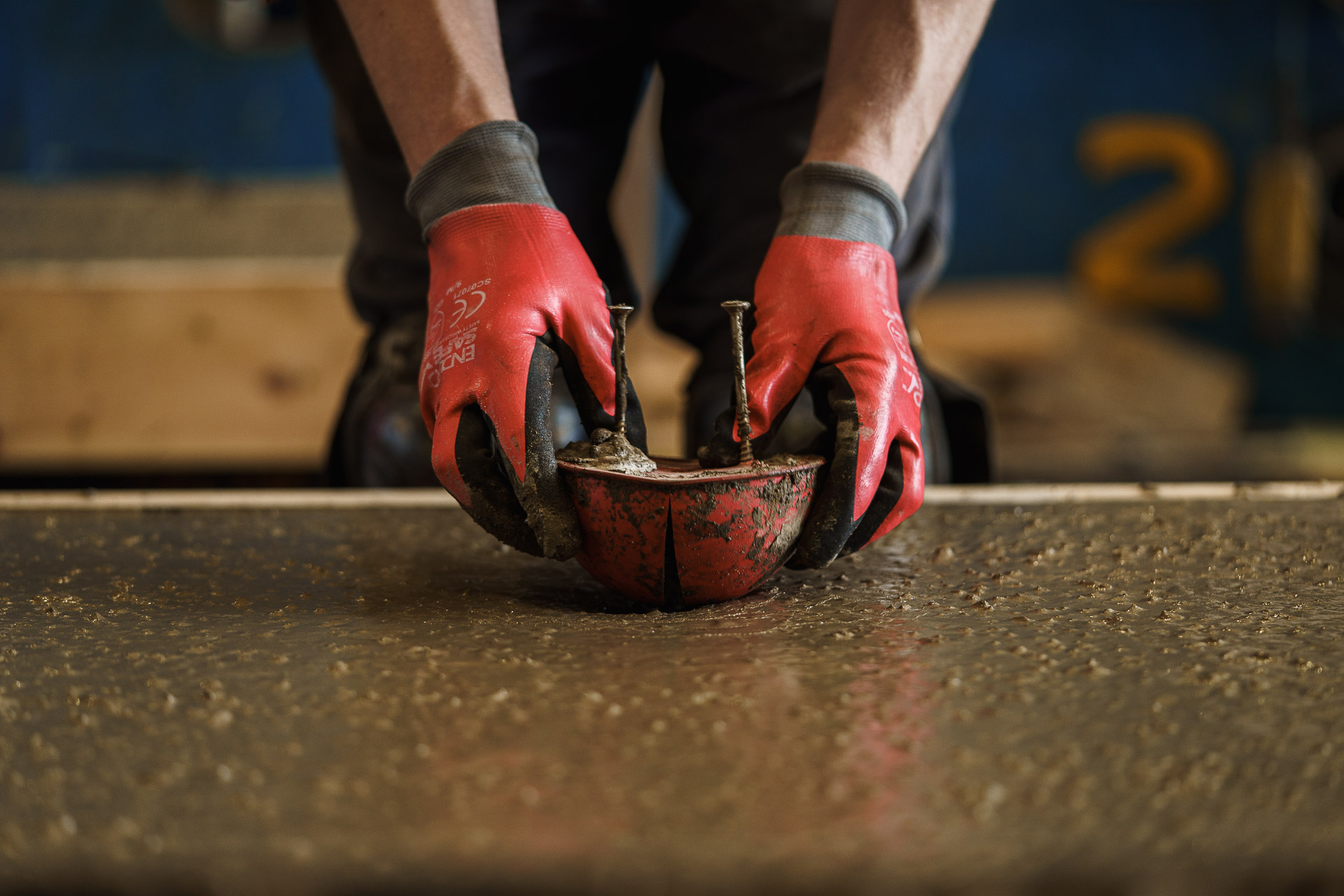 Person wearing red gloves using a red handheld cement tool on a concrete surface.