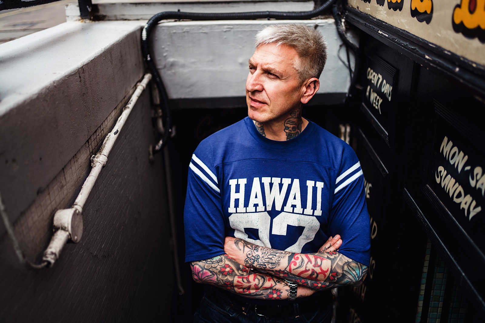street style portrait of man with tatoos stood at top of basement stairs