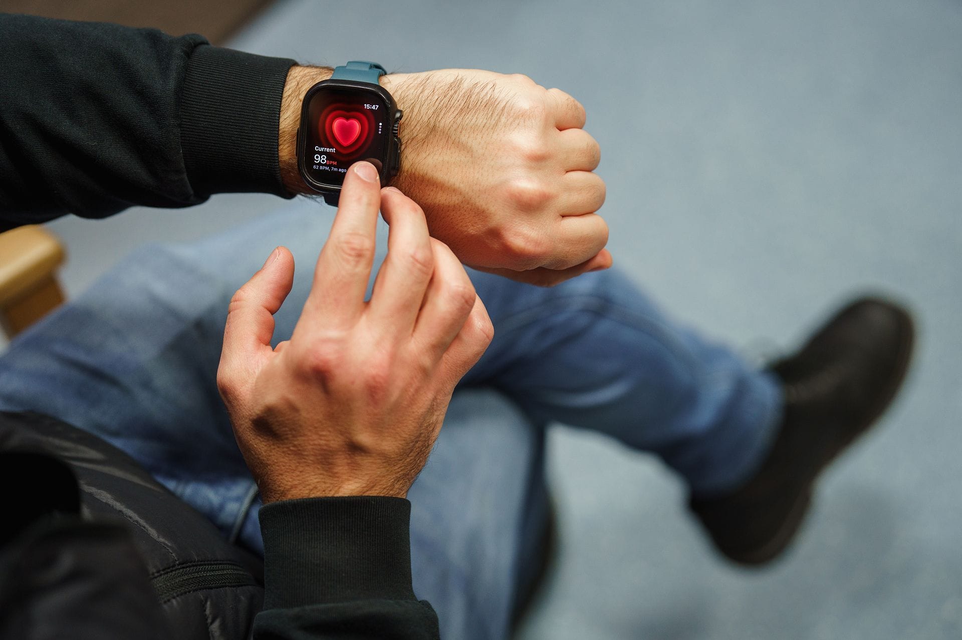 A person sitting and checking their heart rate on a smartwatch, which displays a heart icon and pulse information on the screen.