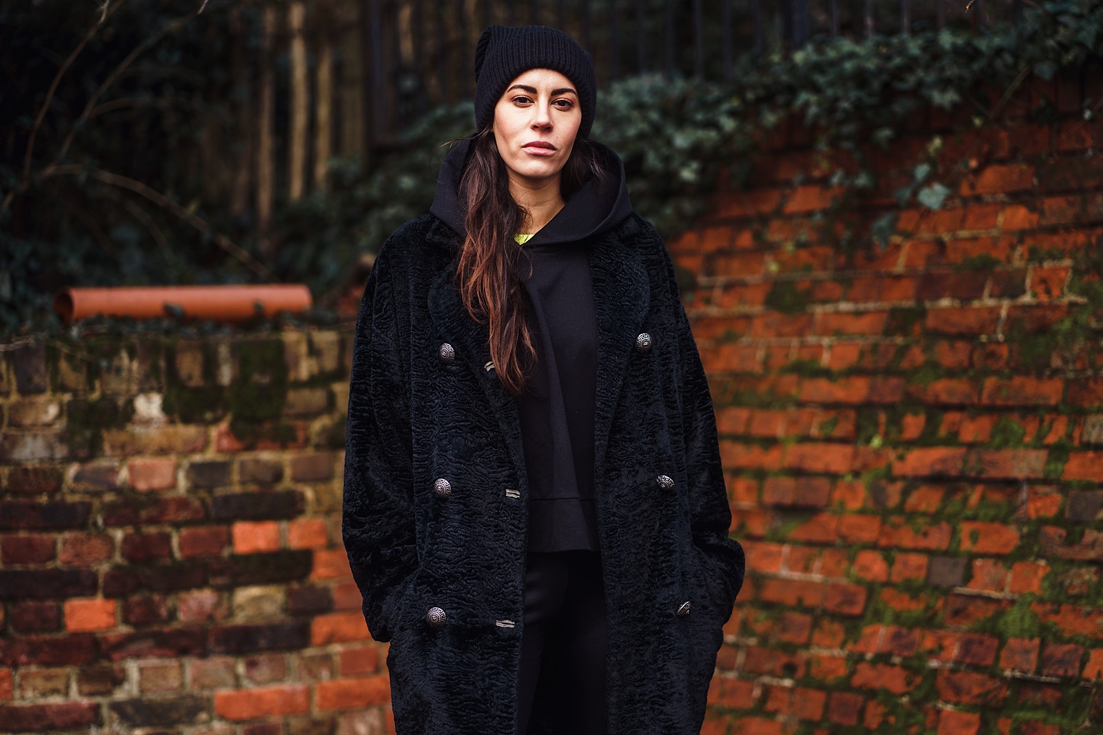 woman all in black stood in front of red brick wall