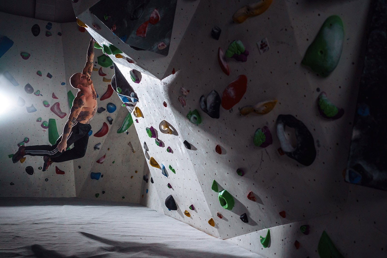 Image of a man hanging from a rock-climbing wall with just one hand
