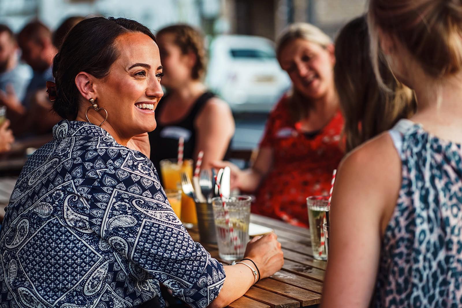 women outside with drinks sat at a table smiling and talking