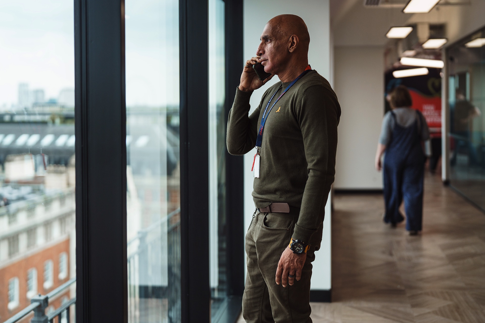 Man in green jumper looking out of a plate glass window whilst talking on his phone