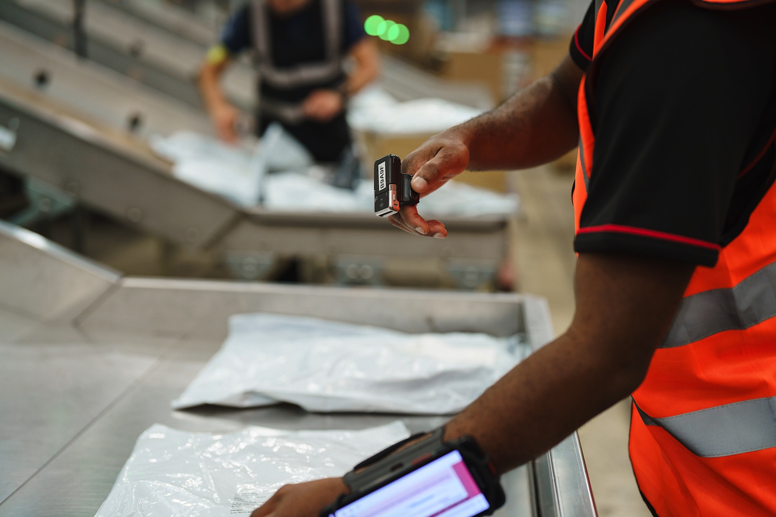 A worker in a high-visibility vest scans a package with a barcode scanner at a sorting facility.