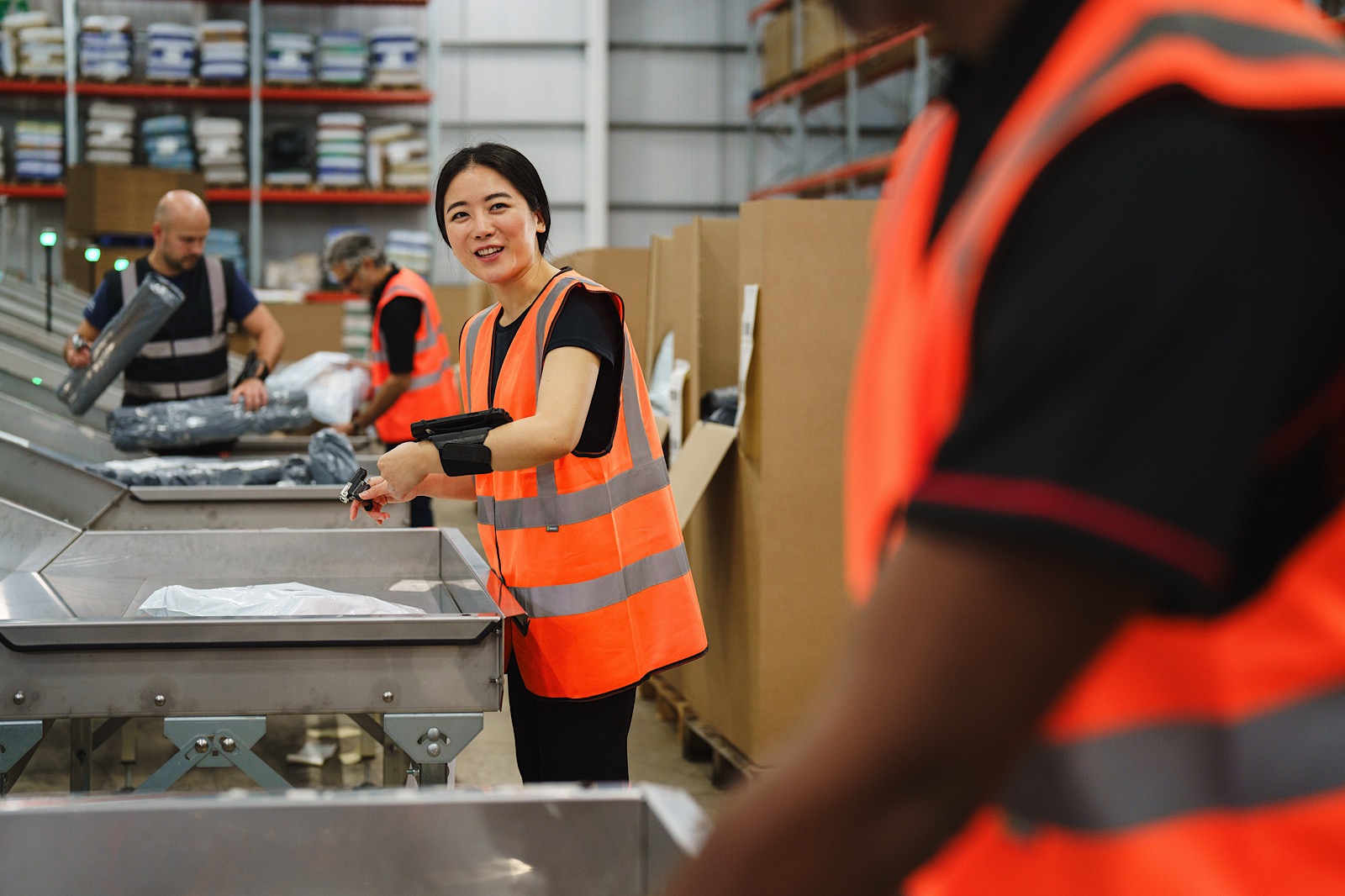 Workers in high-visibility vests sort packages on a conveyor belt in a warehouse setting.