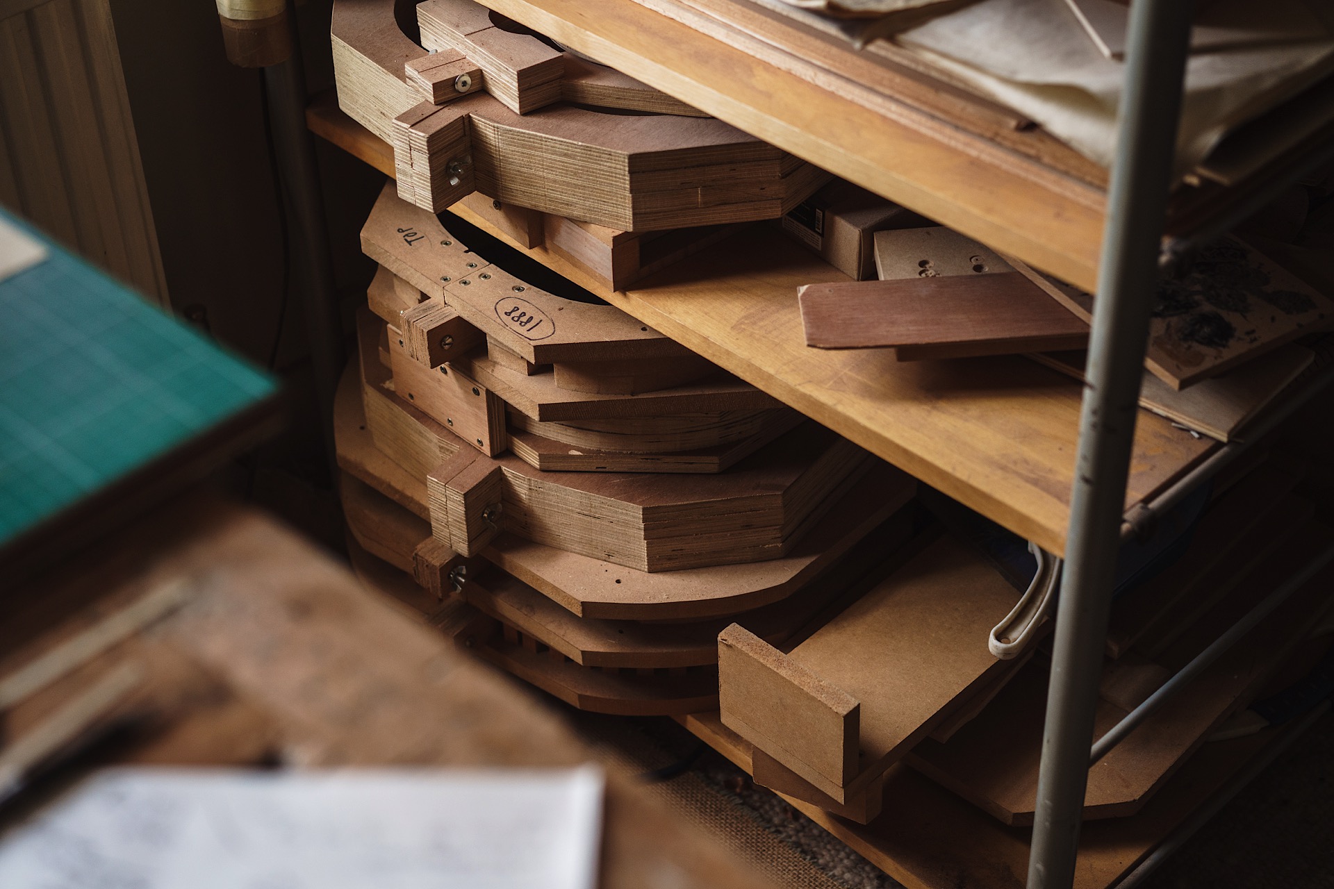 Wooden guitar molds stacked on shelves in a workshop setting.